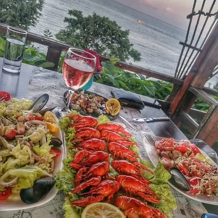 A platter of whole crayfish on lettuce with lemon at Restaurant Breeze, set on a terrace table at sunset beside seafood salads with mussels and a glass of rosé, with the Black Sea behind.