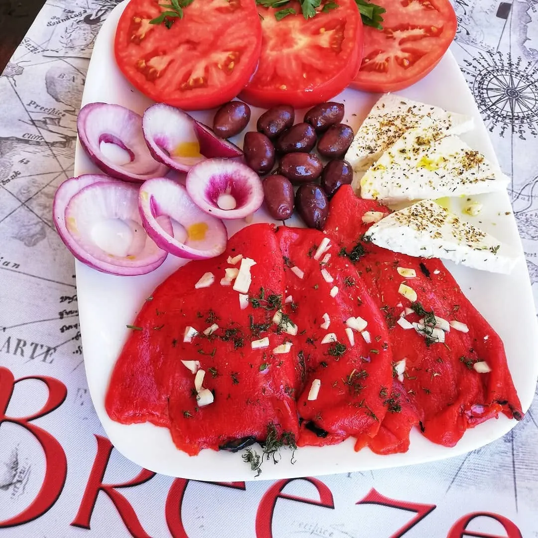 The house salad at Restaurant Breeze on a Breeze-branded placemat: thick tomato slices, red onion rings, kalamata olives, wedges of white brine cheese dusted with oregano, and skinned roasted red peppers with garlic and dill.