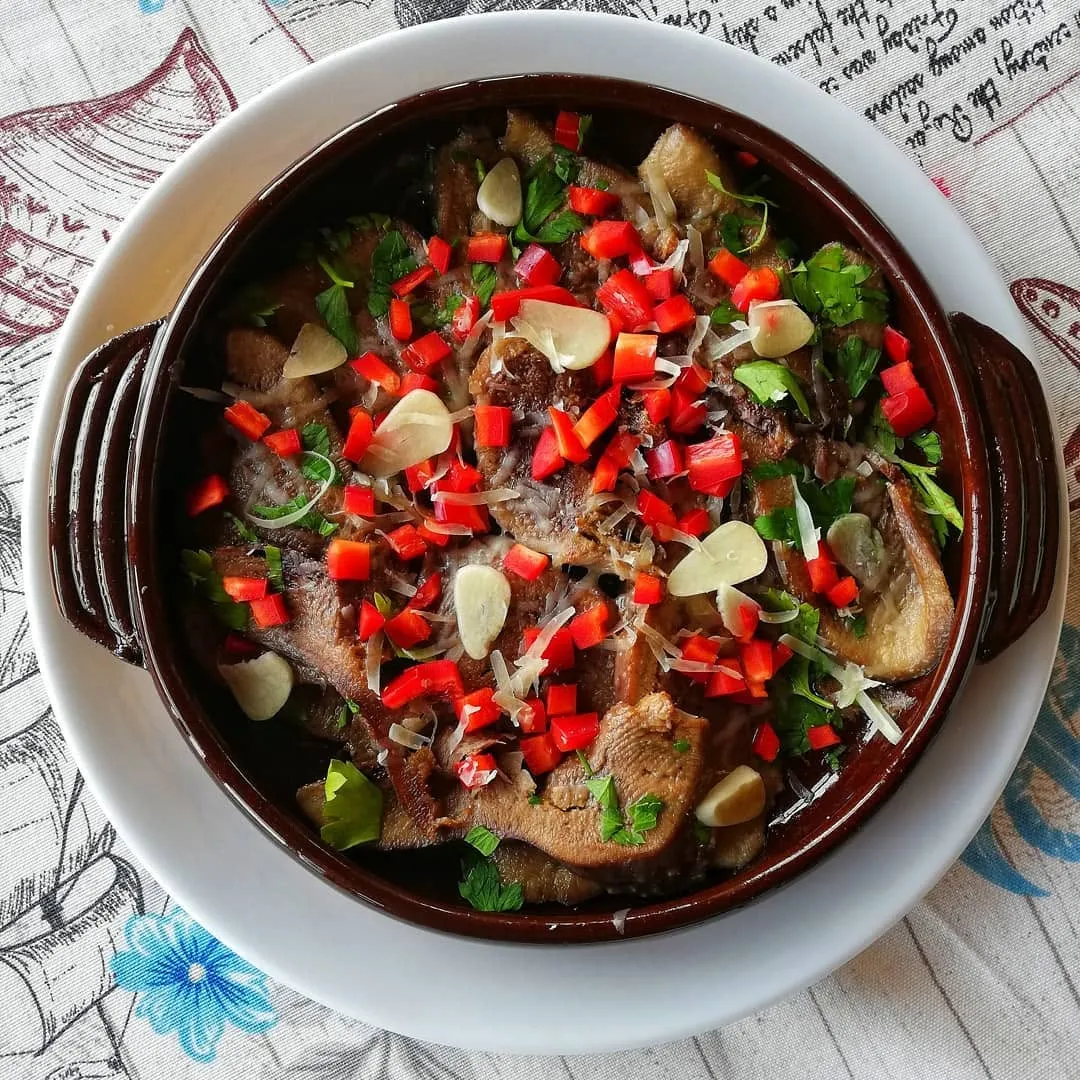Mushrooms in garlic butter at Restaurant Breeze, served in a glazed brown clay dish: sliced mushrooms under melted cheese, scattered with diced red pepper, garlic slivers and flat-leaf parsley.
