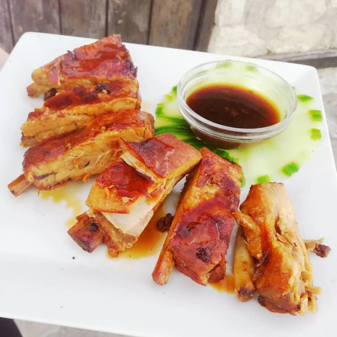 Pork ribs at Restaurant Breeze: a rack sliced into glazed, deeply browned ribs on a white plate, with a small glass bowl of dark dipping sauce and a scattering of chopped spring onion.